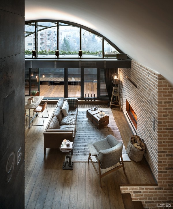 attic-apartment-with-custom-furniture-family-room-with-brick-fireplace-glass-wall-flooring-lamp-custom-paneling-brown-sofa-suitcase-table