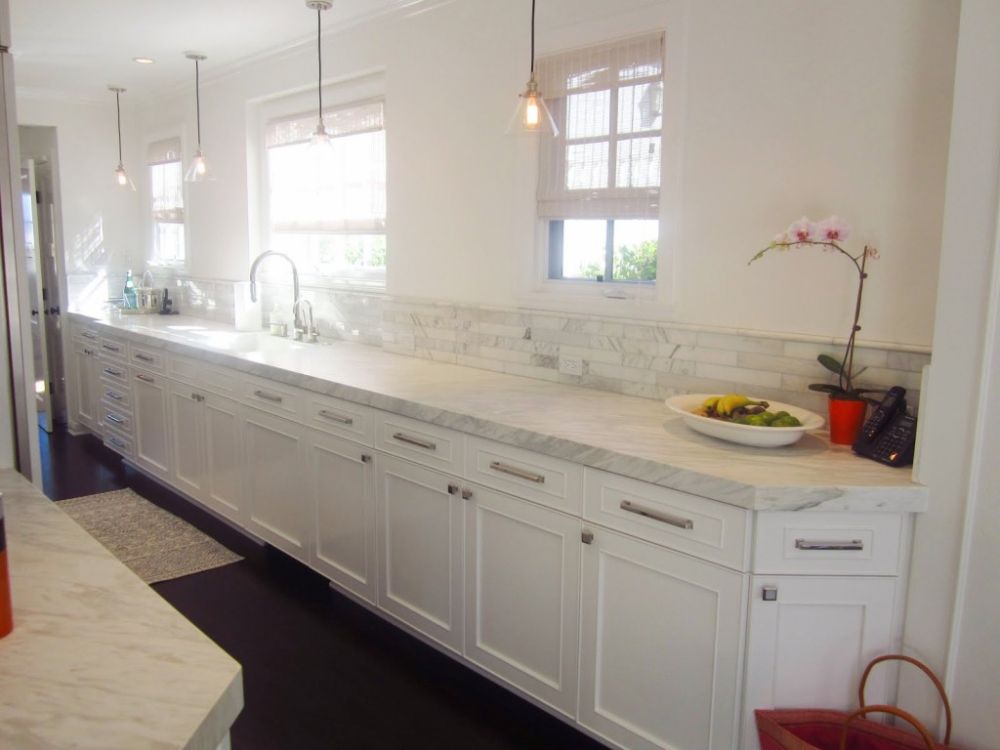 sleek white themed kitchen design with long white cabinetry and cafe pendant lights